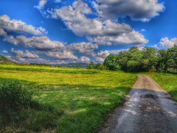 Empty road amidst field against sky