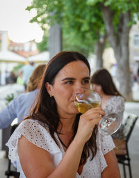 Portrait of happy young woman sitting on terrace of a restaurant, drinking white wine