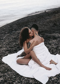 A couple in love spend the night at the sea, kissing and hugging on the beach covered with a blanket