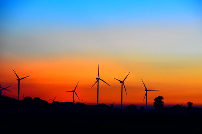 Silhouette wind turbines on field against sky during sunset