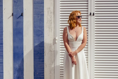 Woman in dress and sunglasses standing against wall