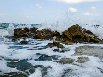 Water splashing on rocks by sea against sky