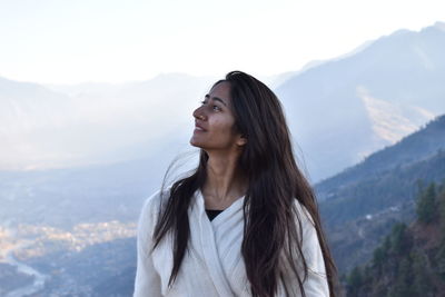 Beautiful young woman looking away against mountains