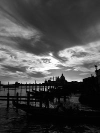 Silhouette of boats in river against cloudy sky