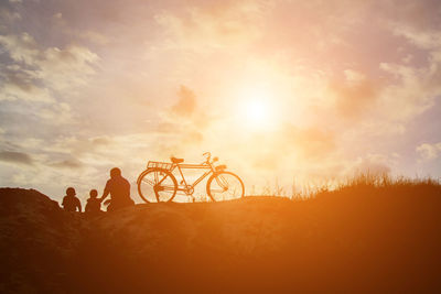 People riding bicycle against sky during sunset