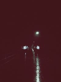 Illuminated street by river against sky at night