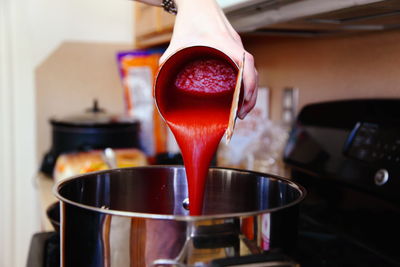 Cropped hand pouring tomato sauce in cooking utensil at home