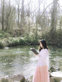 Side view of woman photographing while standing by lake