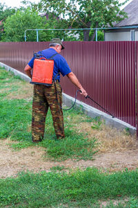 An elderly man sprays ragweed and other weeds with chemicals from a sprayer on a rural street 