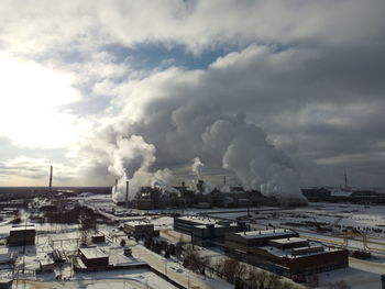 Smoke emitting from factory against cloudy sky