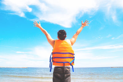 Rear view of man with arms raised standing at beach against sky