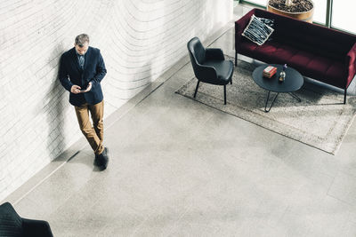 High angle view of mature businessman using mobile phone while standing against wall at office