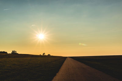 Road amidst field against sky during sunset