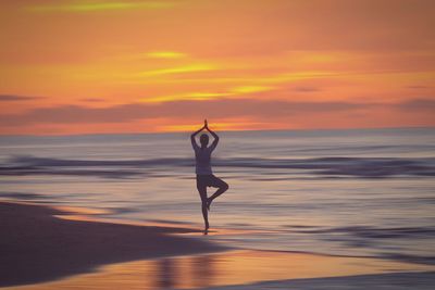 Woman doing yoga at beach during sunset