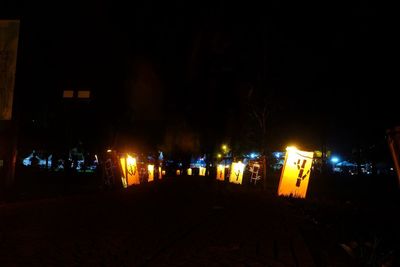 Illuminated street by buildings in city at night