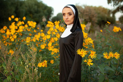 Portrait of young woman standing amidst yellow flowering plants