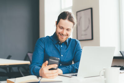 Smiling young man using mobile phone at office