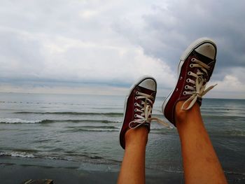 Low section of person wearing shoes against sea