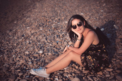 Portrait of young woman wearing sunglasses lying on pebbles