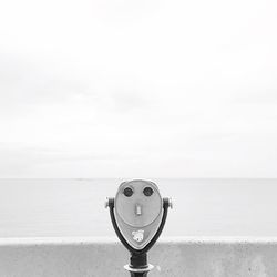 Close-up of coin-operated binoculars by sea against sky