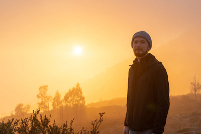 Young man standing against sky during sunset