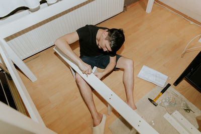 A young man hand screws a screw into a hole in the side of a bunk bed.