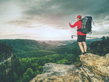 Hiker hold smart phone on the peak of mountain. man in red t-shirt and shorts takes photos on peak 