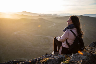 Side view of woman sitting on rock against mountain