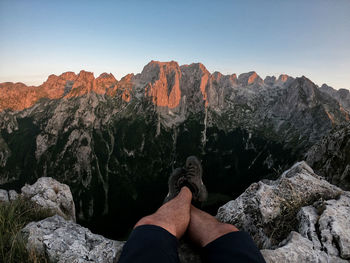 Low section of person on rock in mountains against sky