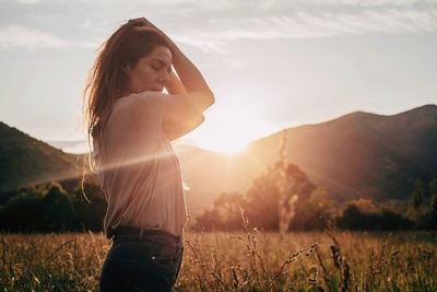 Young woman standing on field against sky during sunset