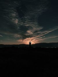 Silhouette man standing on landscape against sky at sunset