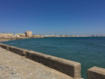 Sea by cityscape against clear blue sky