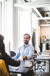 Businessman smiling while giving card to female entrepreneur at counter in office