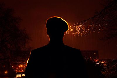 Rear view of silhouette man in front of illuminated building in rainy season