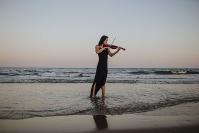 Woman playing violin in front of clear sky at sunset
