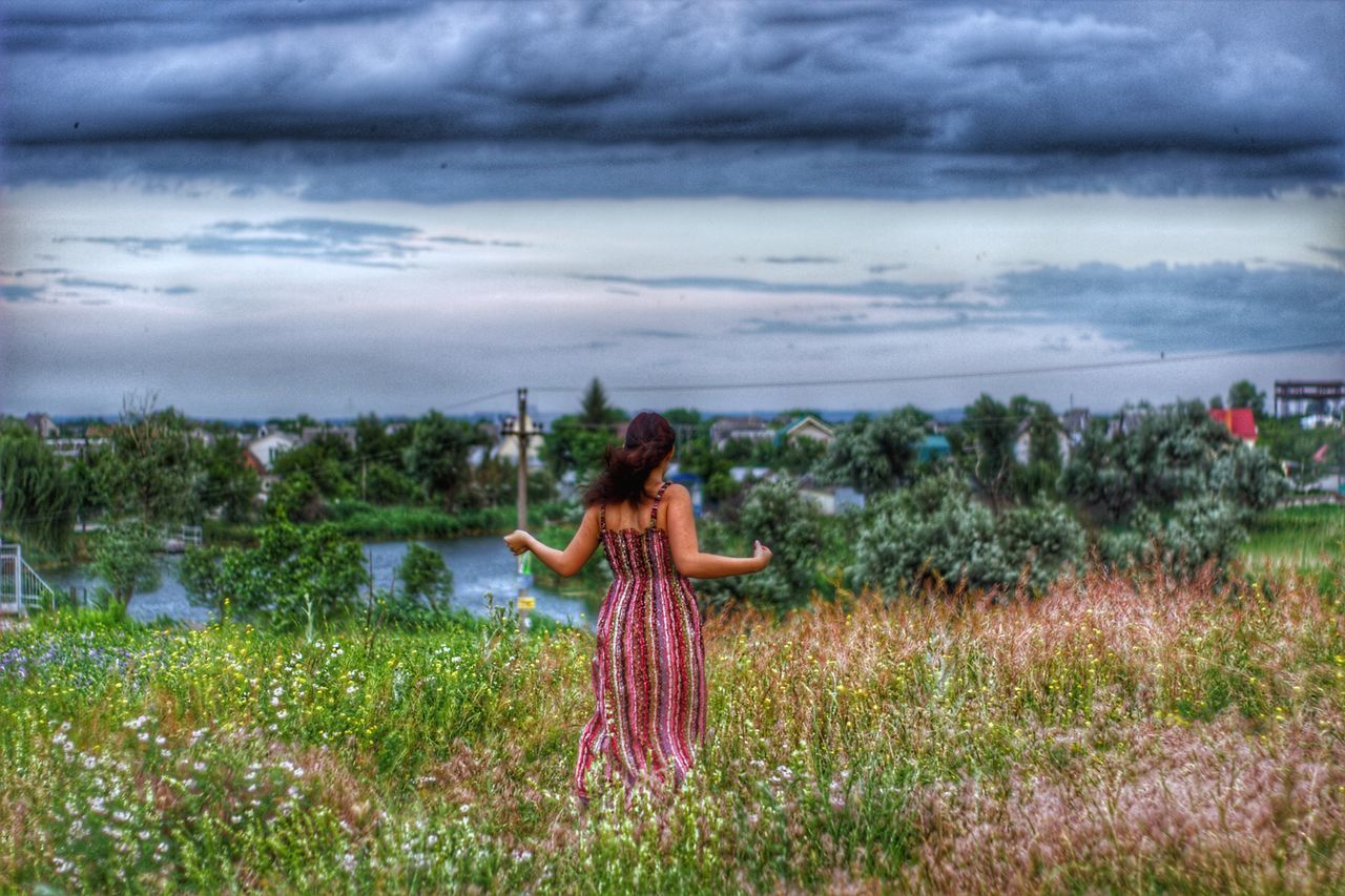 WOMAN WITH UMBRELLA STANDING ON FIELD AGAINST SKY