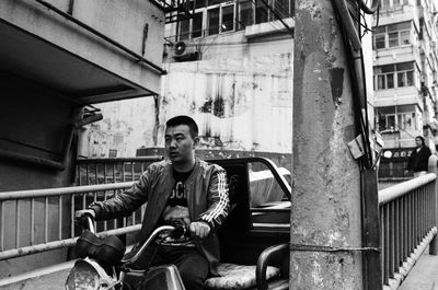 Portrait of young man sitting on railing against building