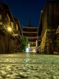 Illuminated street amidst buildings against sky at night