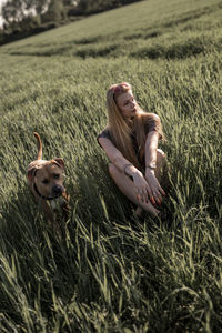 Young woman sitting by dog on grassy field