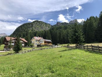 Scenic view of field by trees and houses against sky