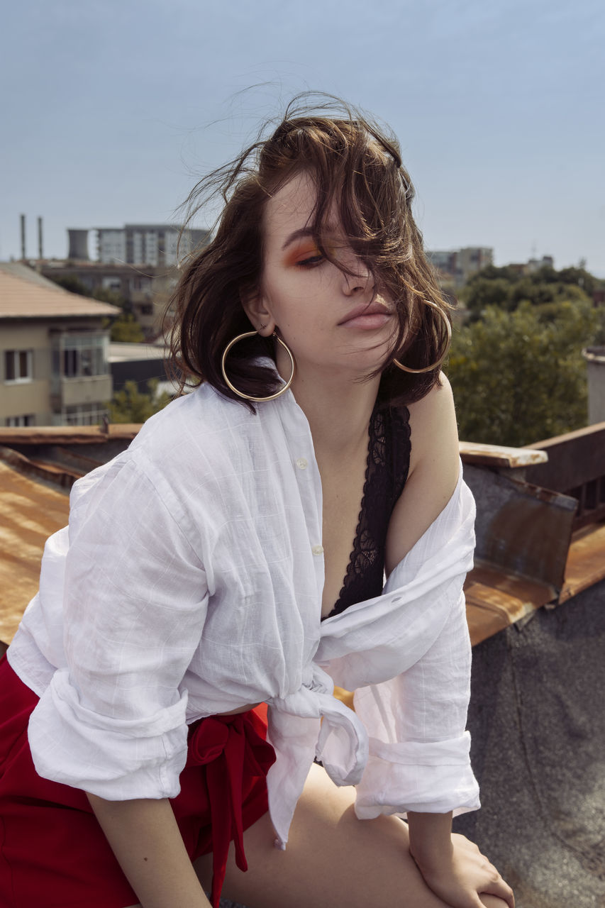 one person, real people, lifestyles, leisure activity, casual clothing, three quarter length, young women, young adult, day, brown hair, architecture, hairstyle, focus on foreground, front view, girls, women, sitting, hair, beautiful woman, outdoors, teenager, contemplation