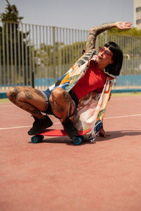 Caucasian girl with tattoos and short black hair on a sports court skating with a skateboard