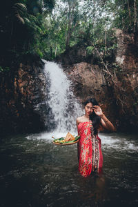 Young woman holding plate while standing in river against waterfall