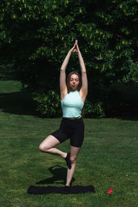 Young caucasian long-haired woman in sportswear is doing yoga in public park. outdoor workout. 