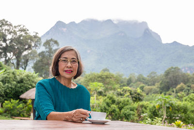 Asin senior woman drinking coffee in cafe outdoor with mountain view