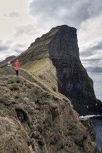 Rear view of man standing on cliff against sky