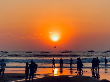 Silhouette people standing on beach against orange sky