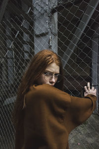 Portrait of young woman standing by chainlink fence