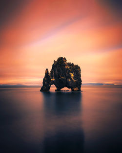 Rock formation in sea against romantic sky at sunset