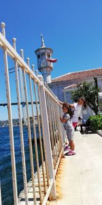 People standing by railing against clear blue sky